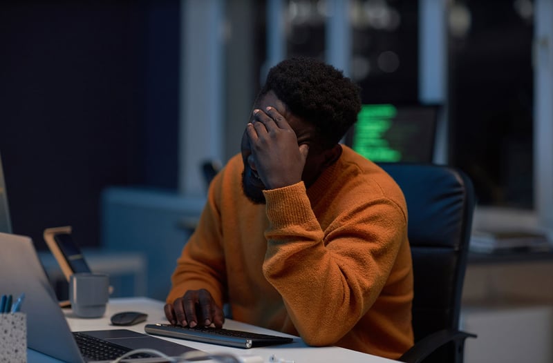 A man sitting with his head in his hands at a desk, representing the challenges of security fatigue faced by SOC teams.